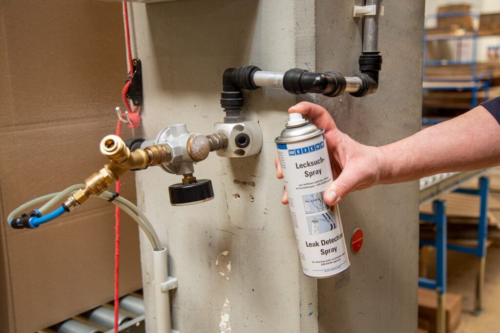 Eine Sprühdose mit Lecksuchspray sprüht auf eine Rohrleitung
