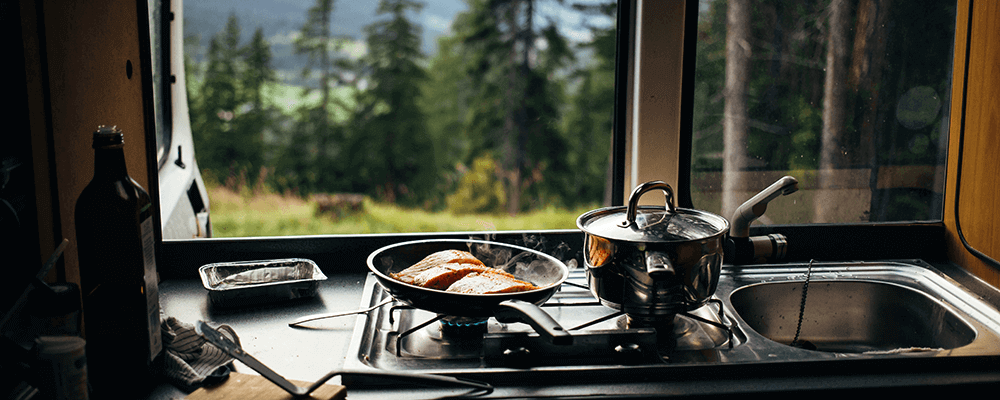 Gros plan sur une poêle à frire avec du saumon biologique préparé à l'intérieur d'un camping-car sur un camping en montagne 